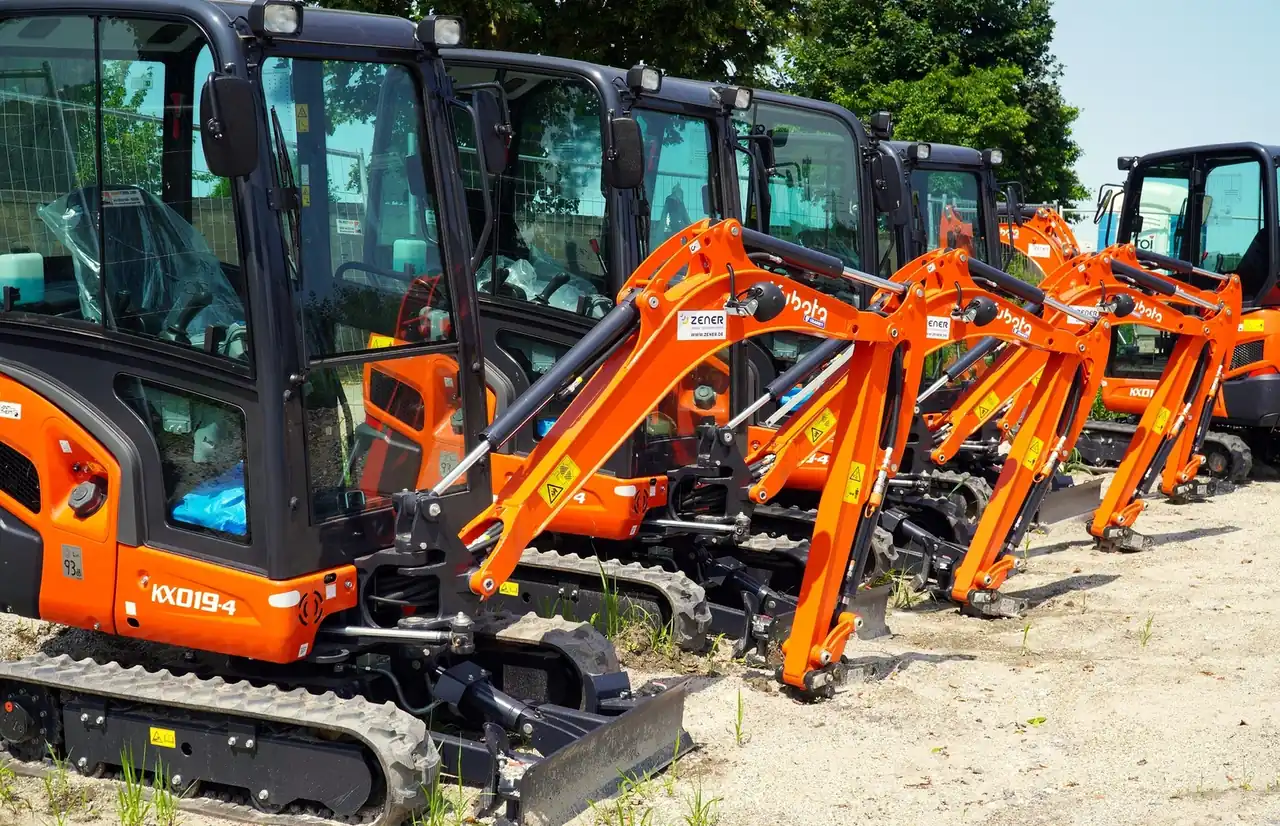 Row of new excavators parked on a sandy yard