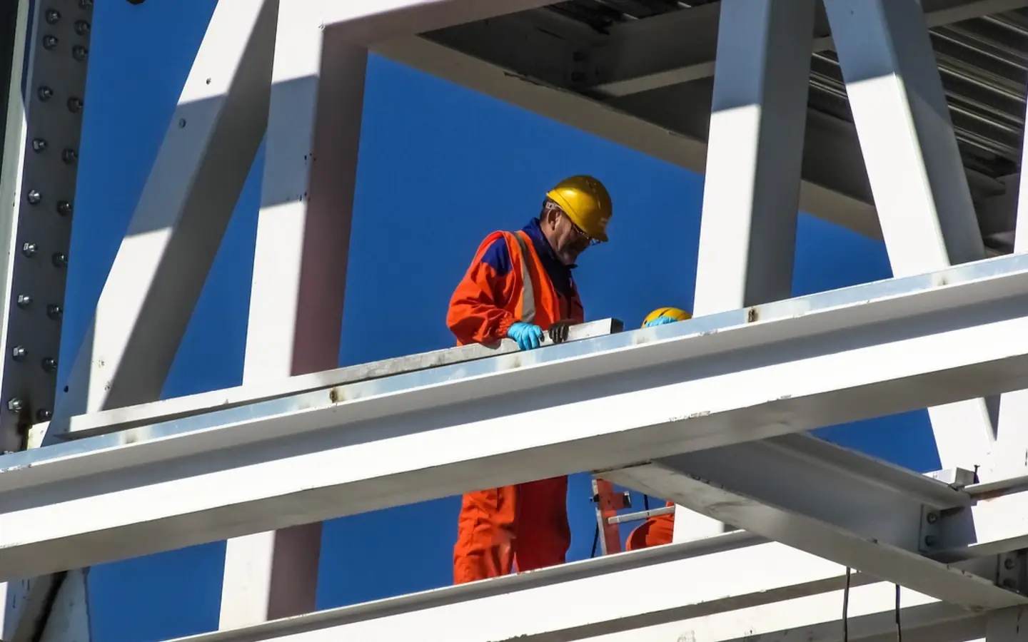Worker in orange coveralls and hard hat on a structural steel frame