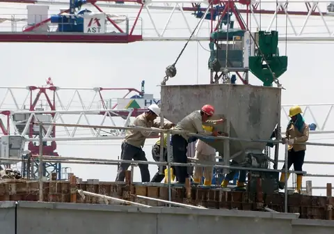 Crew guiding a crane-lifted concrete bucket on a tower deck