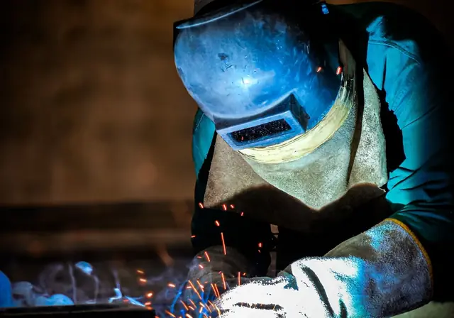 Welder in a helmet and leather gloves at work in a fabrication shop