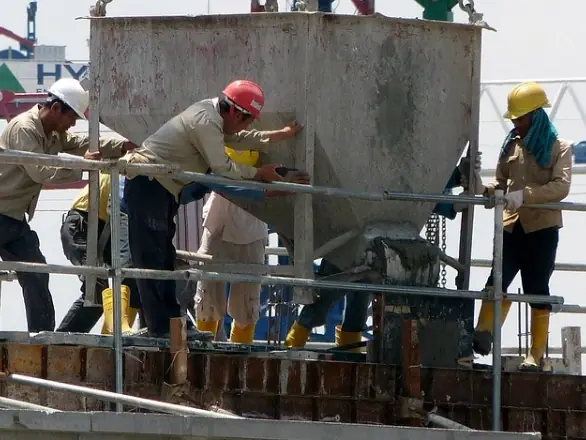 Crew guiding a crane-lifted concrete bucket on a tower deck