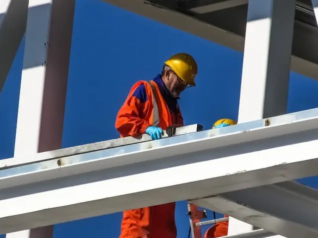 Worker in orange coveralls at height on a structural steel frame
