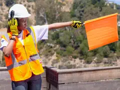 Site worker in a hi-vis vest and hard hat signalling with a flag